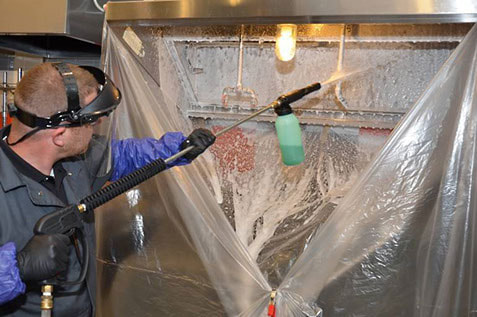 a hood cleaning technician spraying cleaning agent onto a commercial kitchen hood